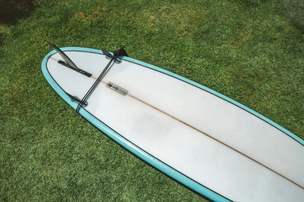 A surfboard rests on lush green grass under bright sunlight, showcasing outdoor lifestyle.